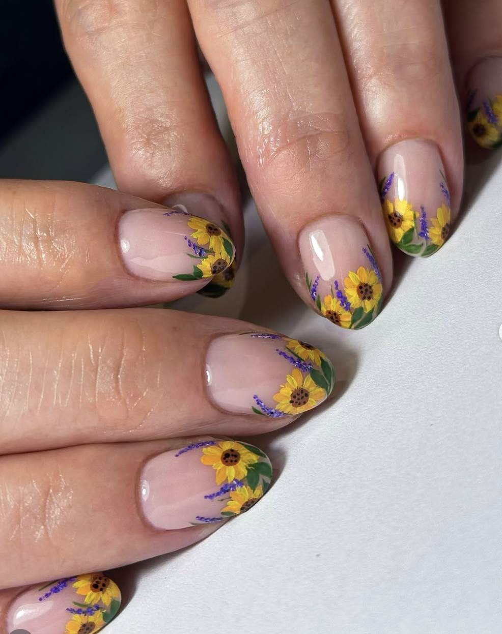 Long almond-shaped nails on a clear base featuring hand-painted sunflowers with yellow petals and small purple lavender sprigs around the edges.
