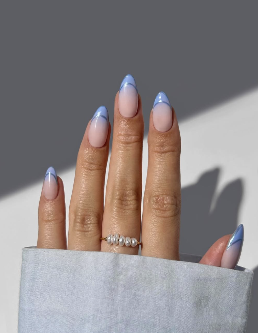 Long almond nails with a soft peach-to-pink gradient base, blue French tips, and a thin darker blue outline tracing the smile line.
