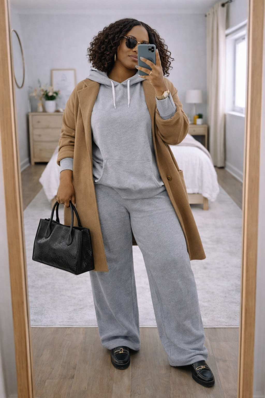 A woman wearing a grey hoodie and matching sweatpants layered under a long, structured camel coat to balance an oversized silhouette.