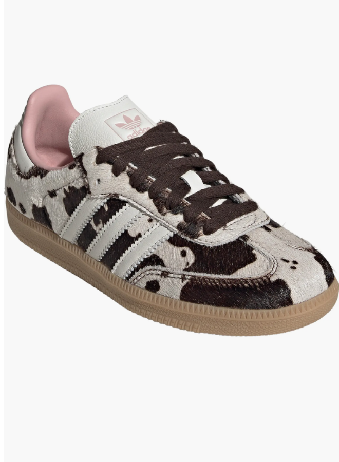 A single Adidas Samba OG sneaker featuring a faux-fur cow print upper, dark brown leather stripes, and a contrasting light pink interior lining, shown against a transparent background.