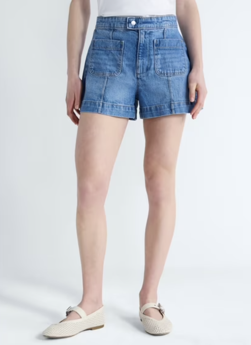 A close-up view of a woman wearing high-waisted, medium-wash denim utility shorts featuring structured front patch pockets and a clean, seamless waistband.