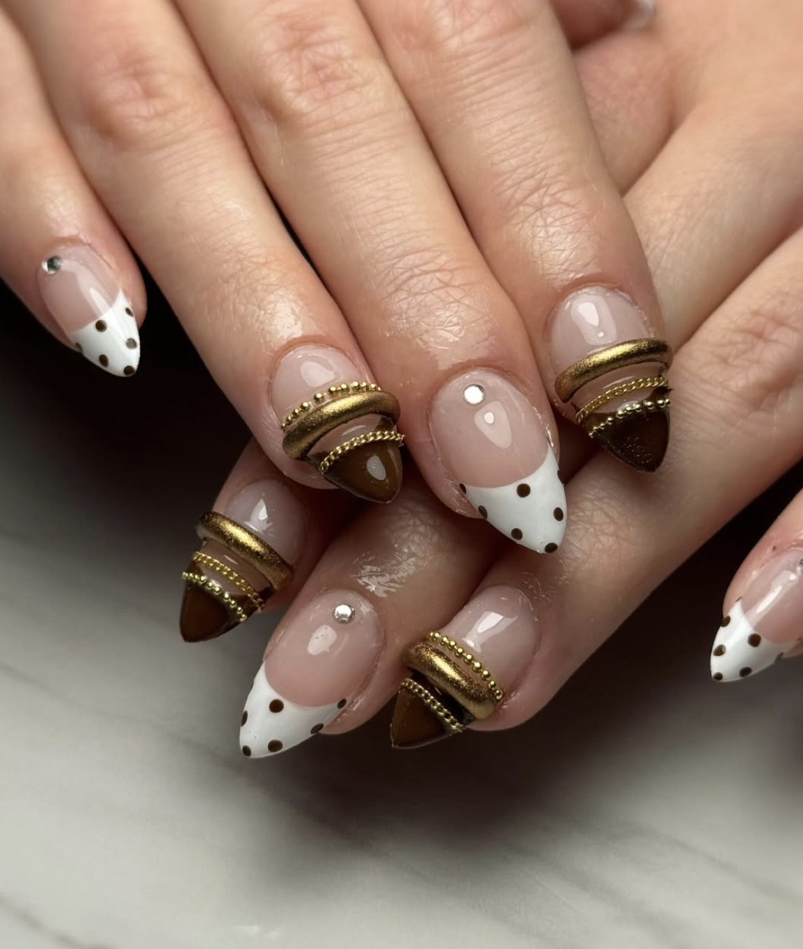 Almond-shaped nails with white French tips, black polka dots, and thick 3D gold textured bangle bands.