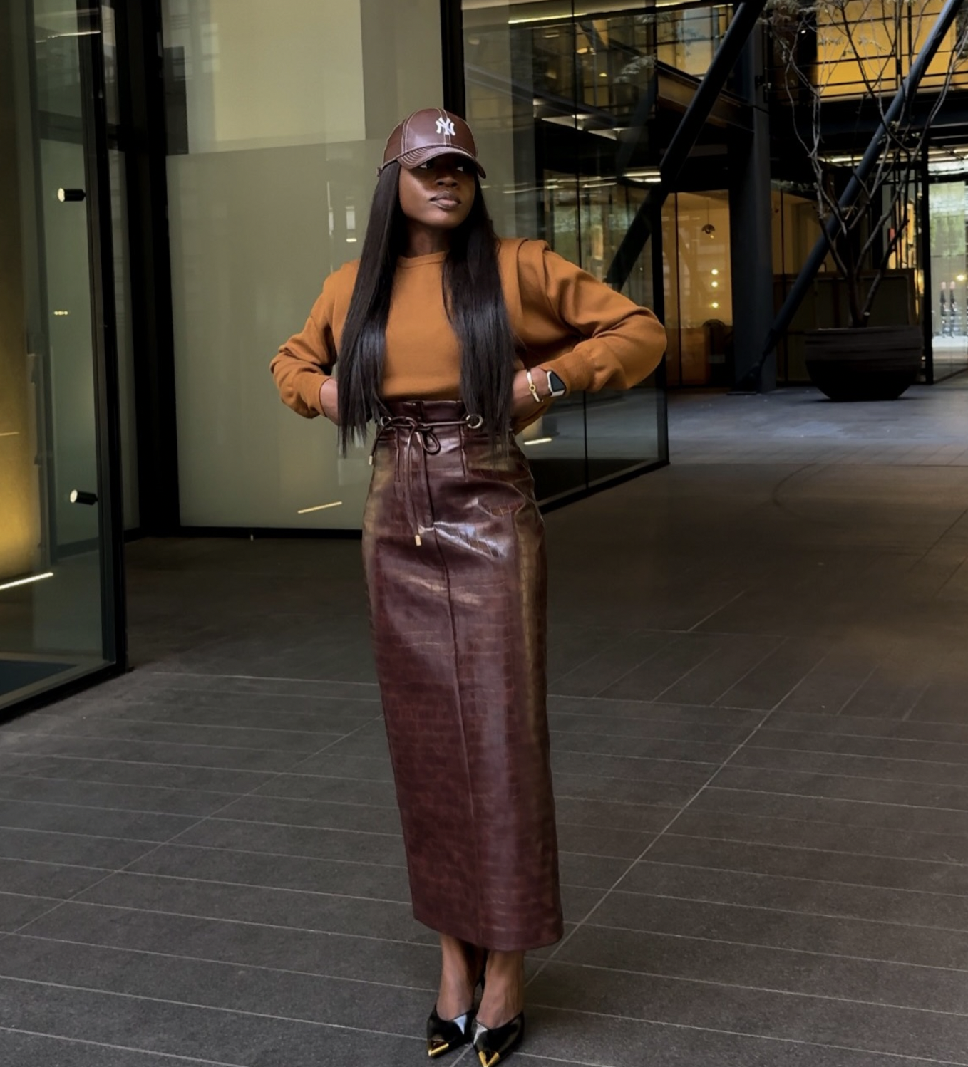 Woman wearing a burgundy croc leather midi skirt with a rust sweater, leather cap and black pointed heels