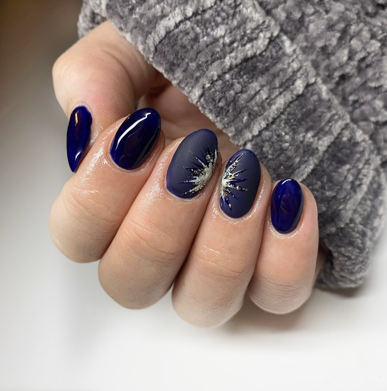 Long, oval-shaped nails showcasing a deep matte navy blue base with a glossy accent nail featuring a high-shine gold and silver metallic firework burst design.