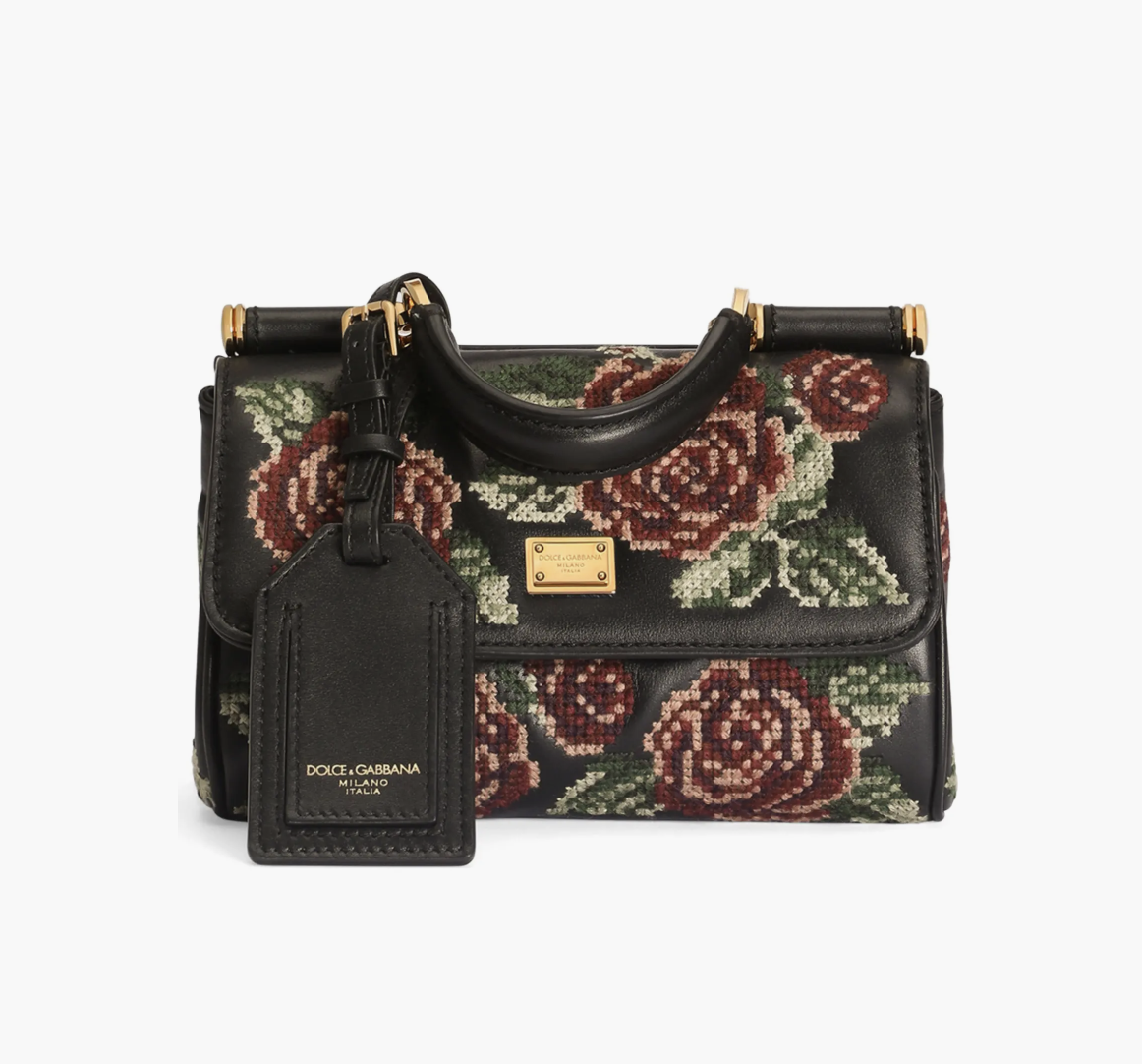 Patterned needlepoint handbag styled with a black sweater dress, tall boots and a long coat.