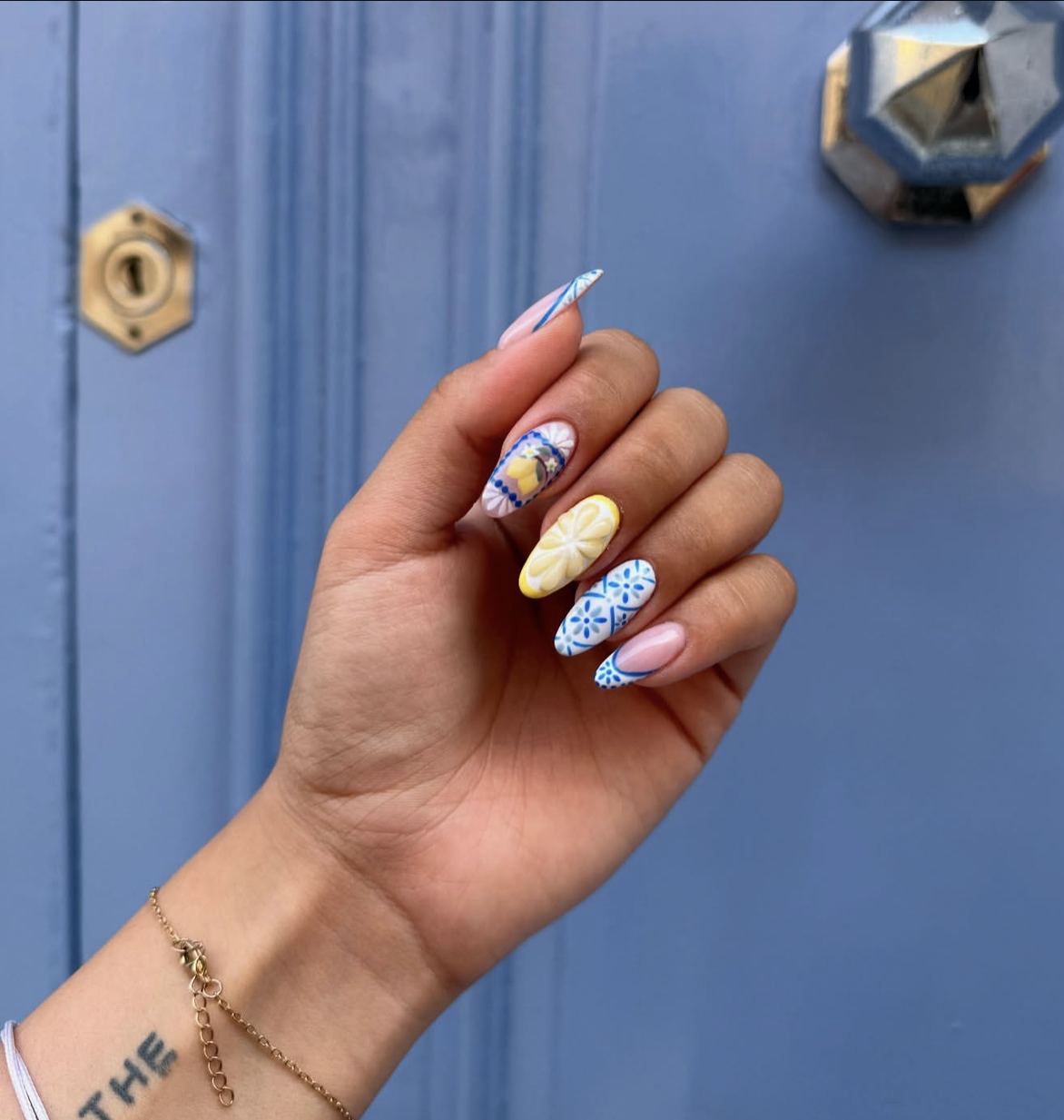 A close-up of a hand with long, oval-shaped nails showcasing intricate Mediterranean tile patterns in royal blue and crisp white