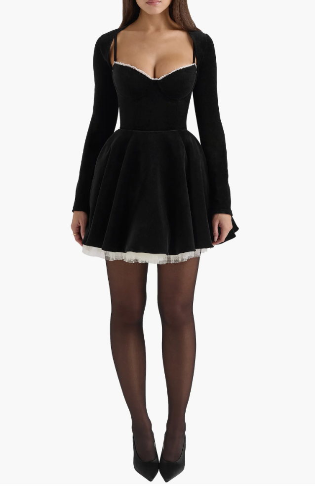 Woman wearing a House of CB Harmony black velvet long-sleeve mini dress paired with sheer black tights and black pointed-toe pumps