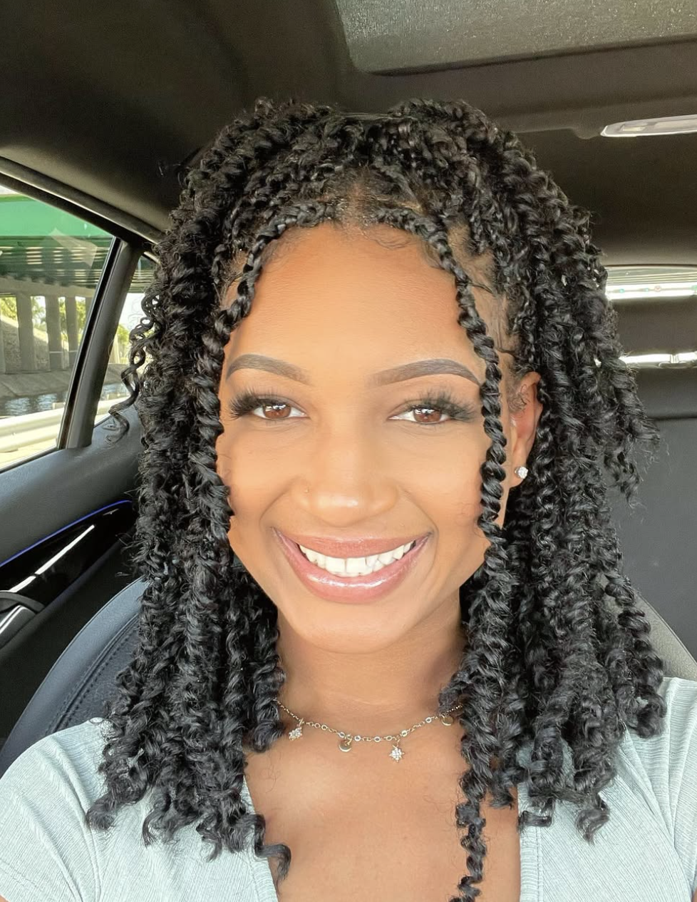 A woman with an oval face shape wearing long, curly passion twists styled in a half-up, half-down look.
