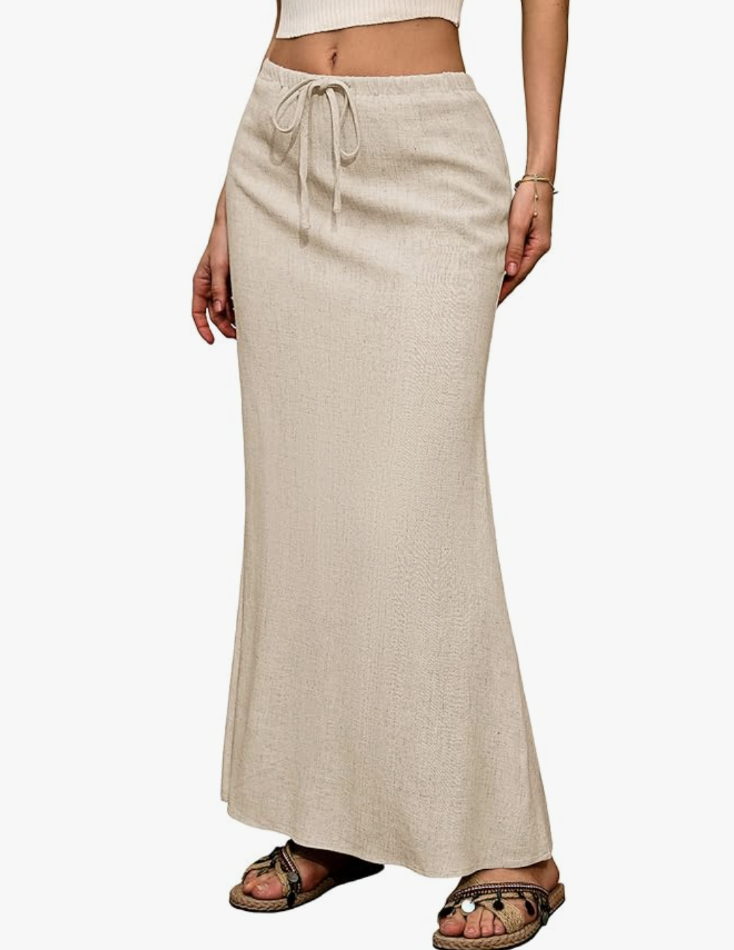 A studio product shot of a woman wearing a high-waisted linen flared maxi skirt in an oatmeal beige color, styled with braided strap sandals.