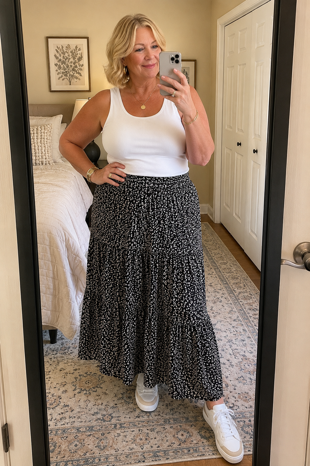 A woman styling a black and white patterned tiered maxi skirt with a tucked-in white tank top and classic low-profile white sneakers.