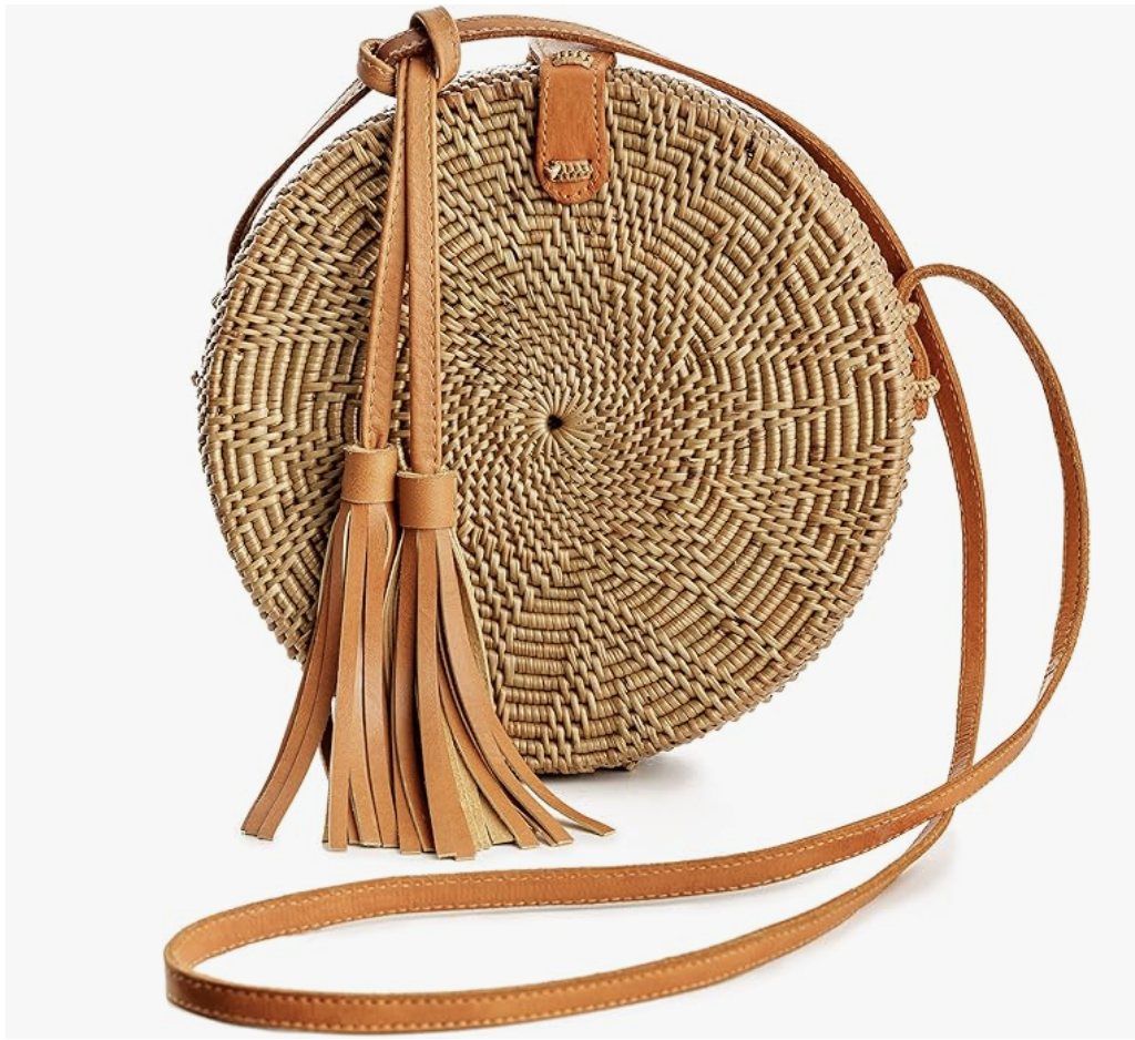 A round, handwoven tan rattan crossbody bag featuring a large decorative leather tassel and a matching tan leather shoulder strap.