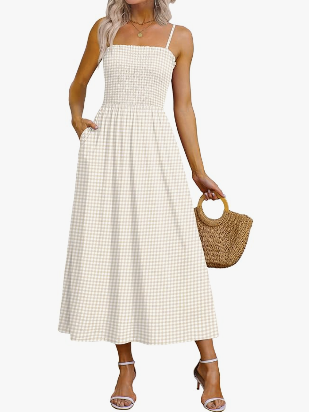 A woman wearing a khaki and white gingham maxi dress with spaghetti straps and a smocked bodice, styled with a small straw bucket bag.