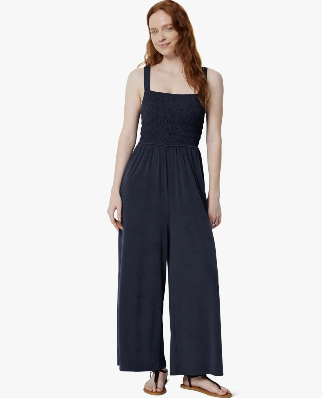 A woman wearing a navy blue sleeveless jumpsuit featuring a flattering square neckline, smocked bodice, and relaxed wide-leg silhouette.