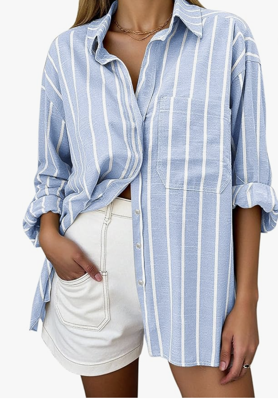 A close-up view of a casual summer outfit featuring an unbuttoned, oversized light blue and white striped linen button-down shirt layered over high-waisted white shorts with distinct pocket details.