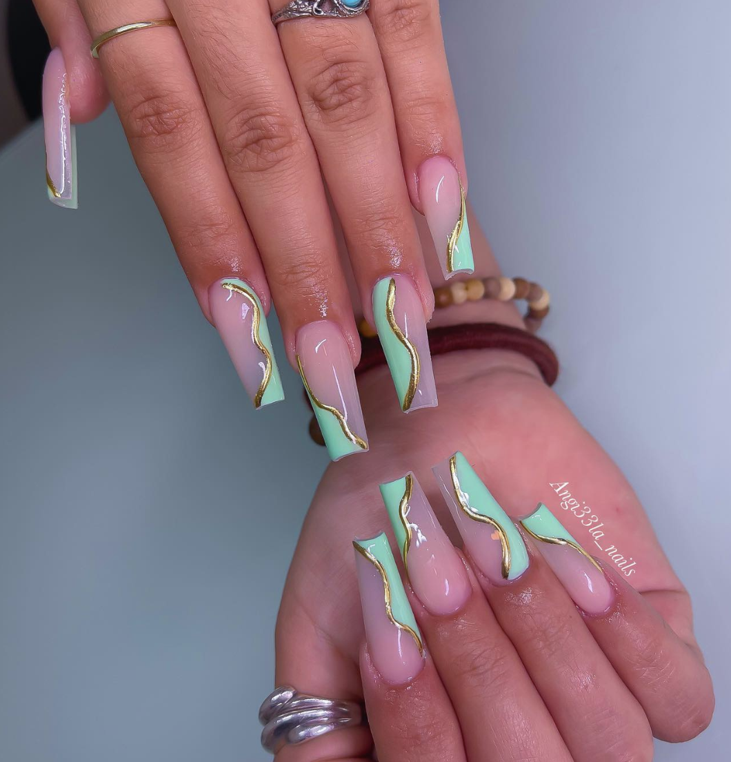 A close-up of long, square nails featuring a mint green marble design with wavy gold chrome accents.