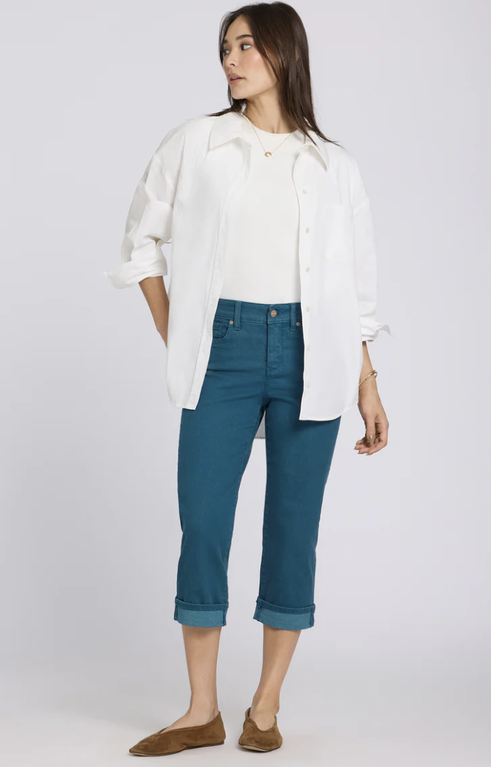 A woman wearing medium-wash NYDJ Marilyn Straight Crop Jeans paired with brown pointed-toe flats. These high-rise stretch jeans feature a slimming front panel and a classic straight-leg cropped silhouette.