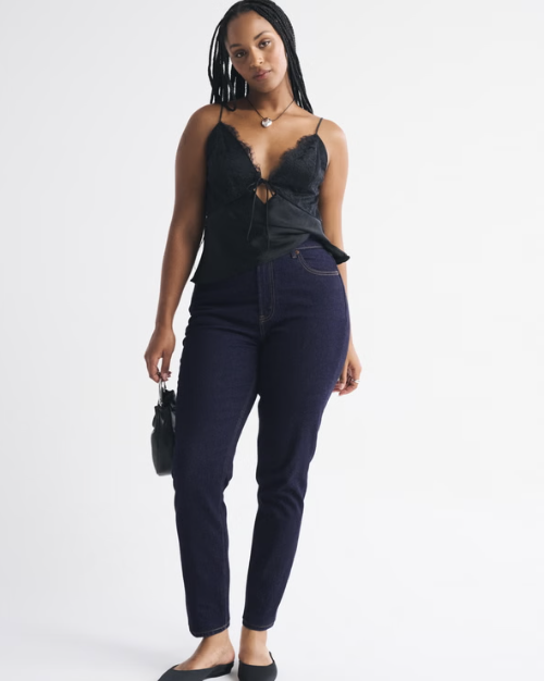 A person with an hourglass figure wearing Abercrombie Curve Love high-rise modern skinny jeans in a dark wash, styled with black ballet flats to show the gap-free waistband and contoured fit through the hips and thighs.