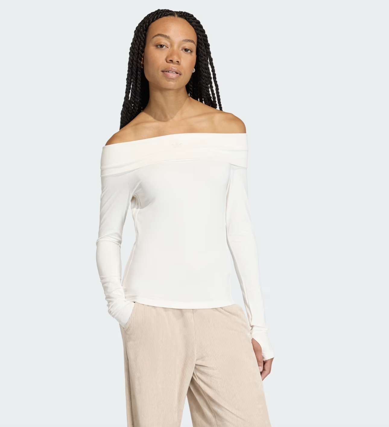 A woman with braided hair wearing a ribbed white off-the-shoulder long-sleeve top styled with beige casual trousers.