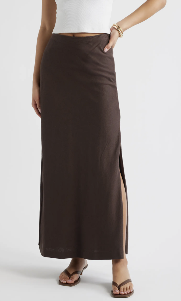 Close-up of a chocolate brown column maxi skirt with a high side slit, styled with brown thong heeled sandals.