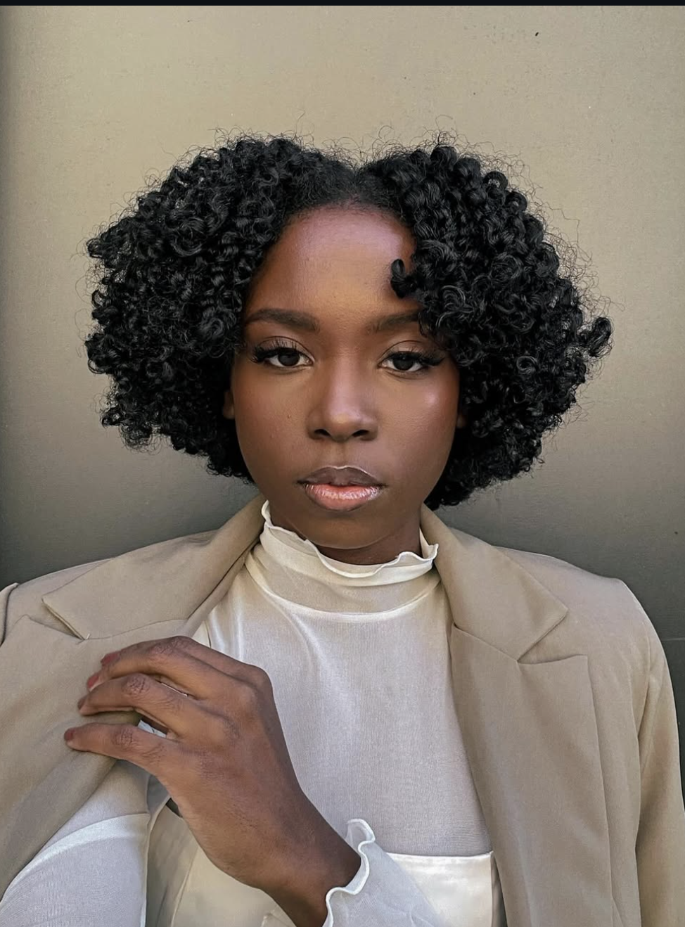 A close-up portrait of a woman showcasing a voluminous and highly defined braid-out bob hairstyle with tight, bouncy curls framing her face.