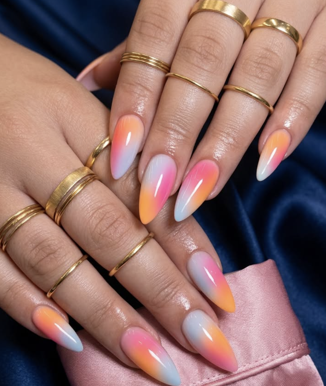 A close-up of long, almond-shaped nails featuring a vibrant vertical aura gradient of neon pink, bright orange, and sky blue, heavily accessorized with multiple stacked thin gold rings.