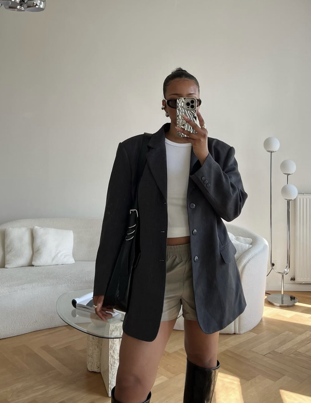 A woman wearing a charcoal grey oversized blazer with matching tailored shorts and tall black boots, demonstrating a chic transitional outfit formula.
