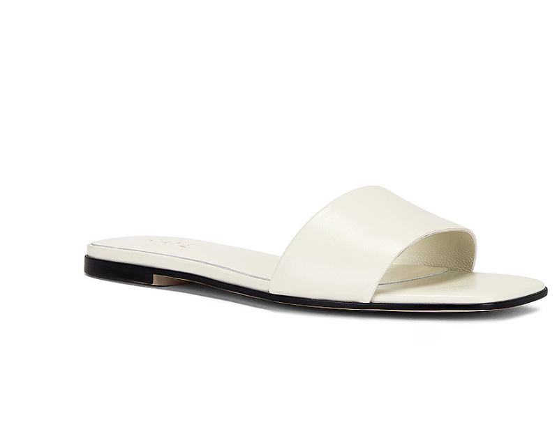 A pair of minimalist white leather slide sandals with a low block heel, perfect for a versatile resort-casual outfit.