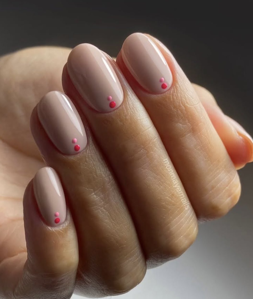 Medium oval-shaped nails with a glossy pale pink base coat, featuring two tiny hot pink micro-dots stacked vertically near the cuticles.