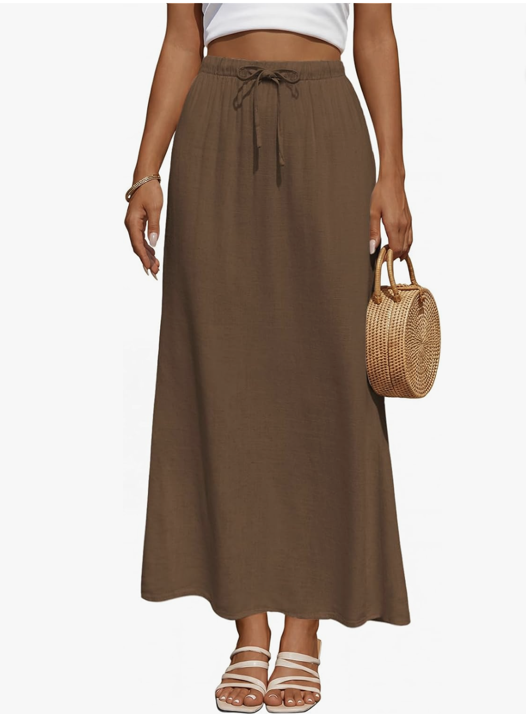 A close-up view of a casual summer look featuring a high-waisted, flowy brown linen maxi skirt with a drawstring waist and side pockets, paired with a white top and strappy flat sandals.