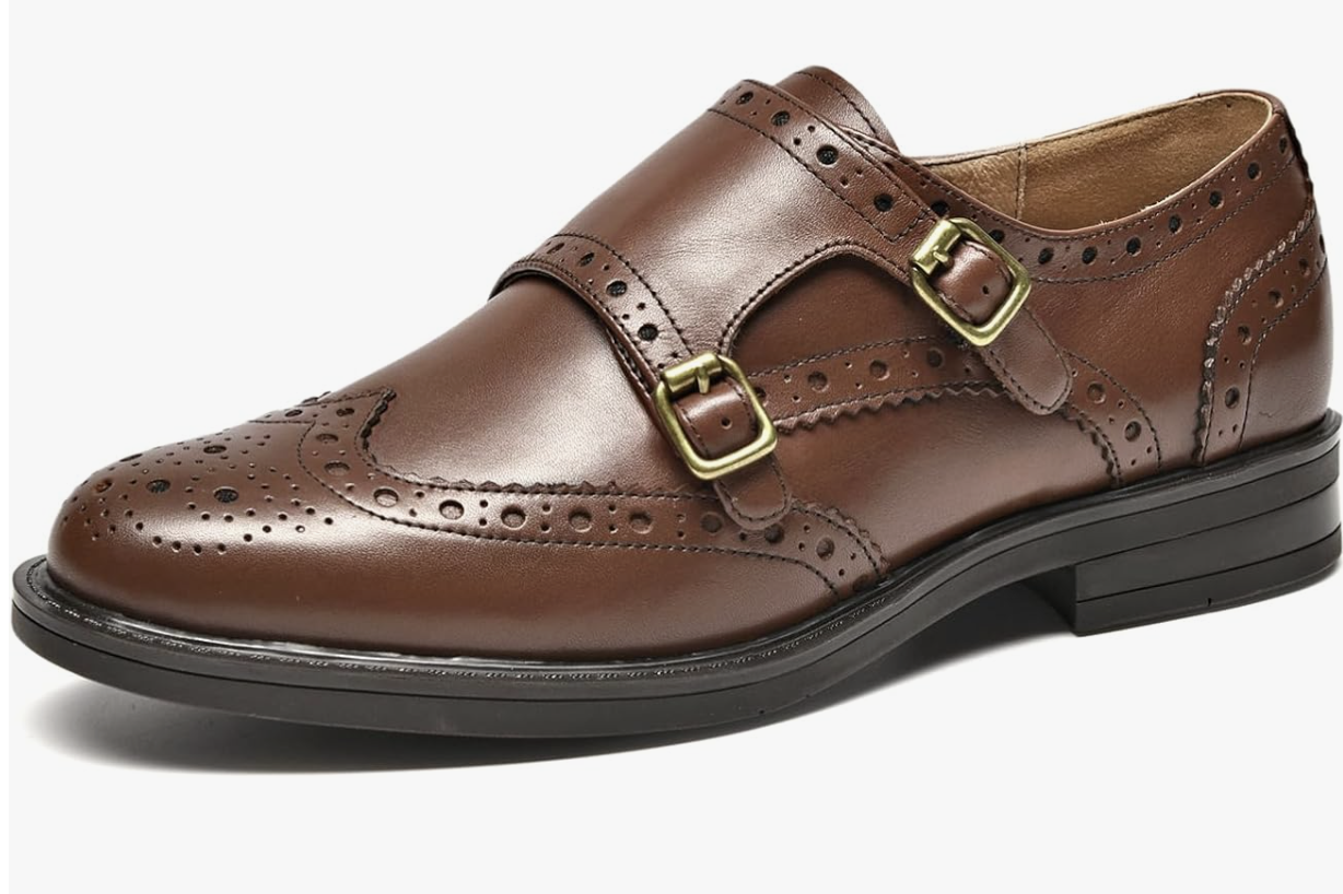 A pair of polished brown leather monk-strap loafers with silver buckle detailing and brogue perforated accents, representing the modern jazz and derby shoe trend for Spring 2026.