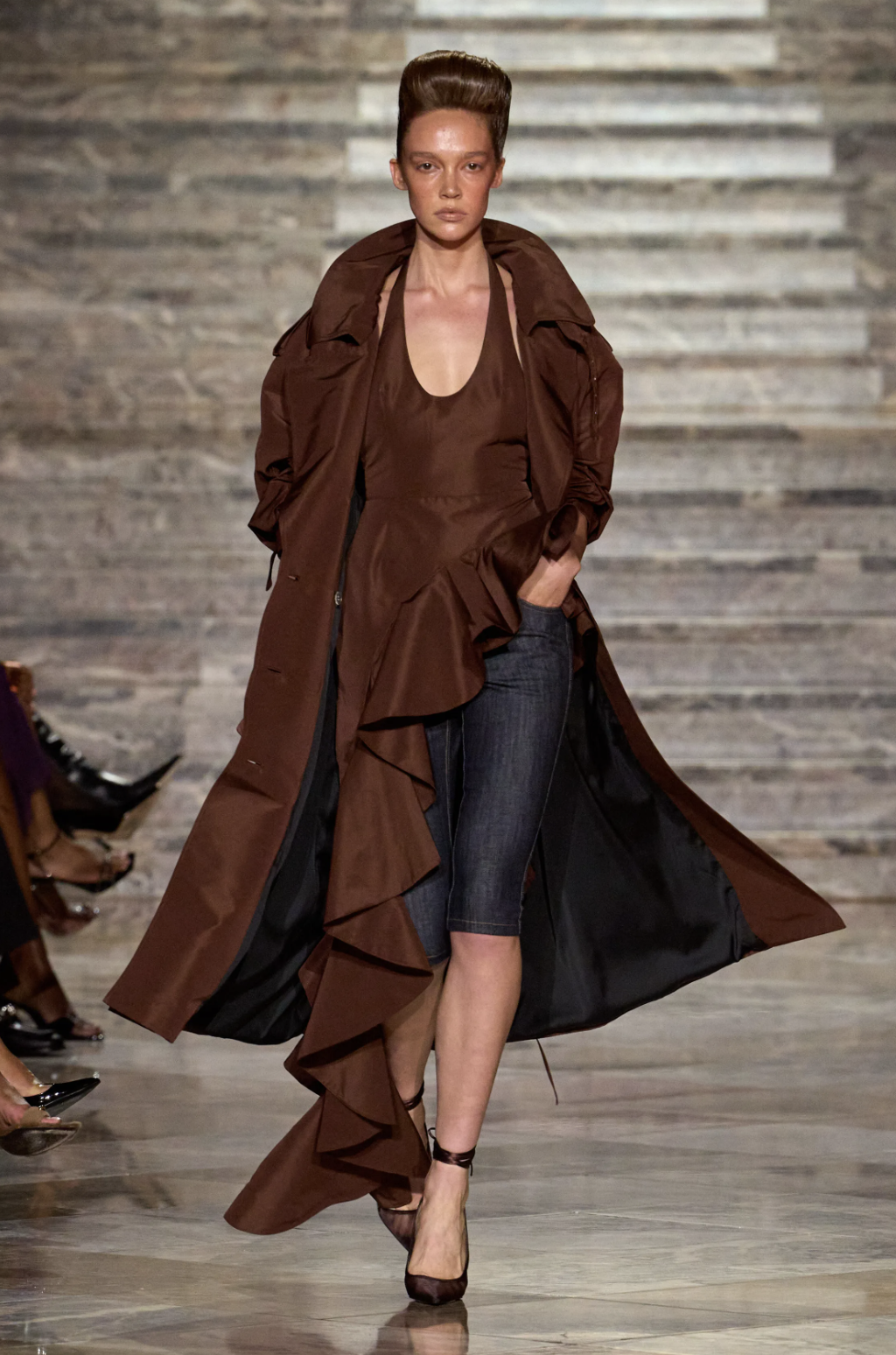 LaQuan Smith Spring 2027 long brown trench over a ruffled top and knee-length denim shorts