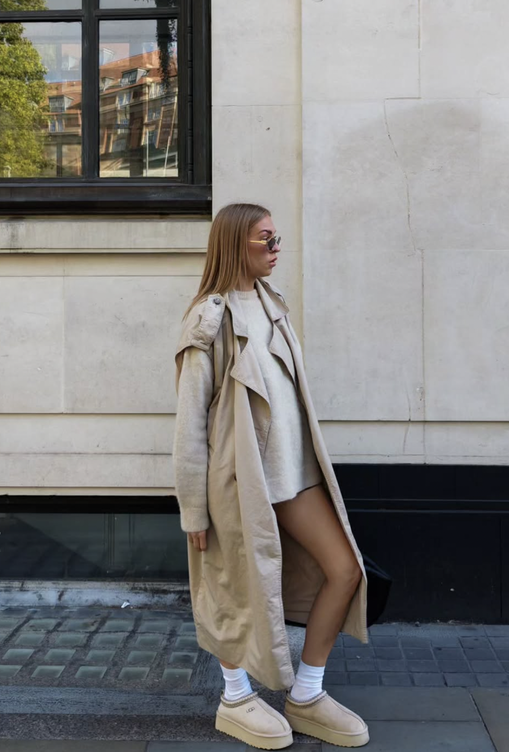 Long beige trench over a short gray outfit with white socks and cream platform slippers.