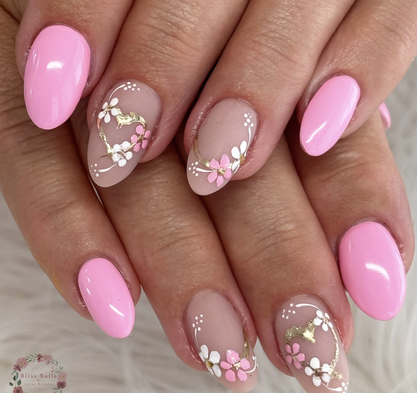 Almond-shaped pink gel nails featuring accent nails with white and pink flowers, gold foil, and a delicate heart-shaped vine.