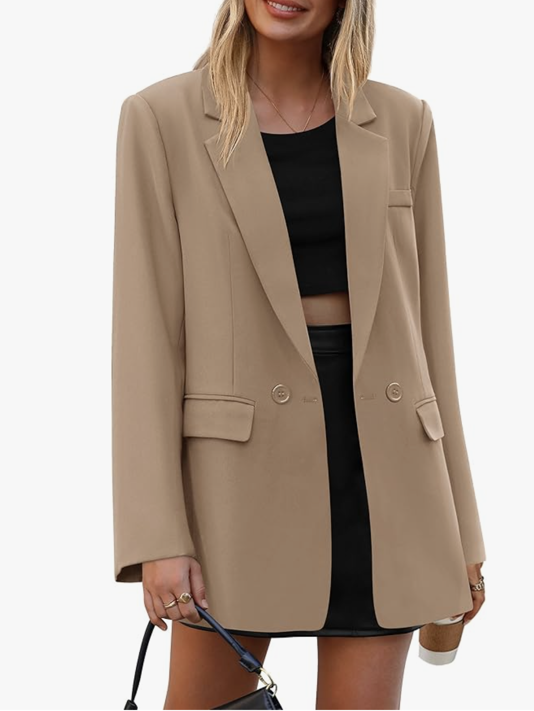 Front view of a woman wearing a tan casual boxy long-sleeve blazer over a black mini dress, accessorized with gold rings and a black shoulder bag.