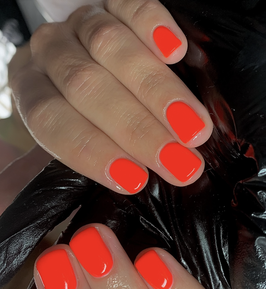 A vibrant, saturated orange manicure on short natural nails, a trending summer 2026 nail colour.