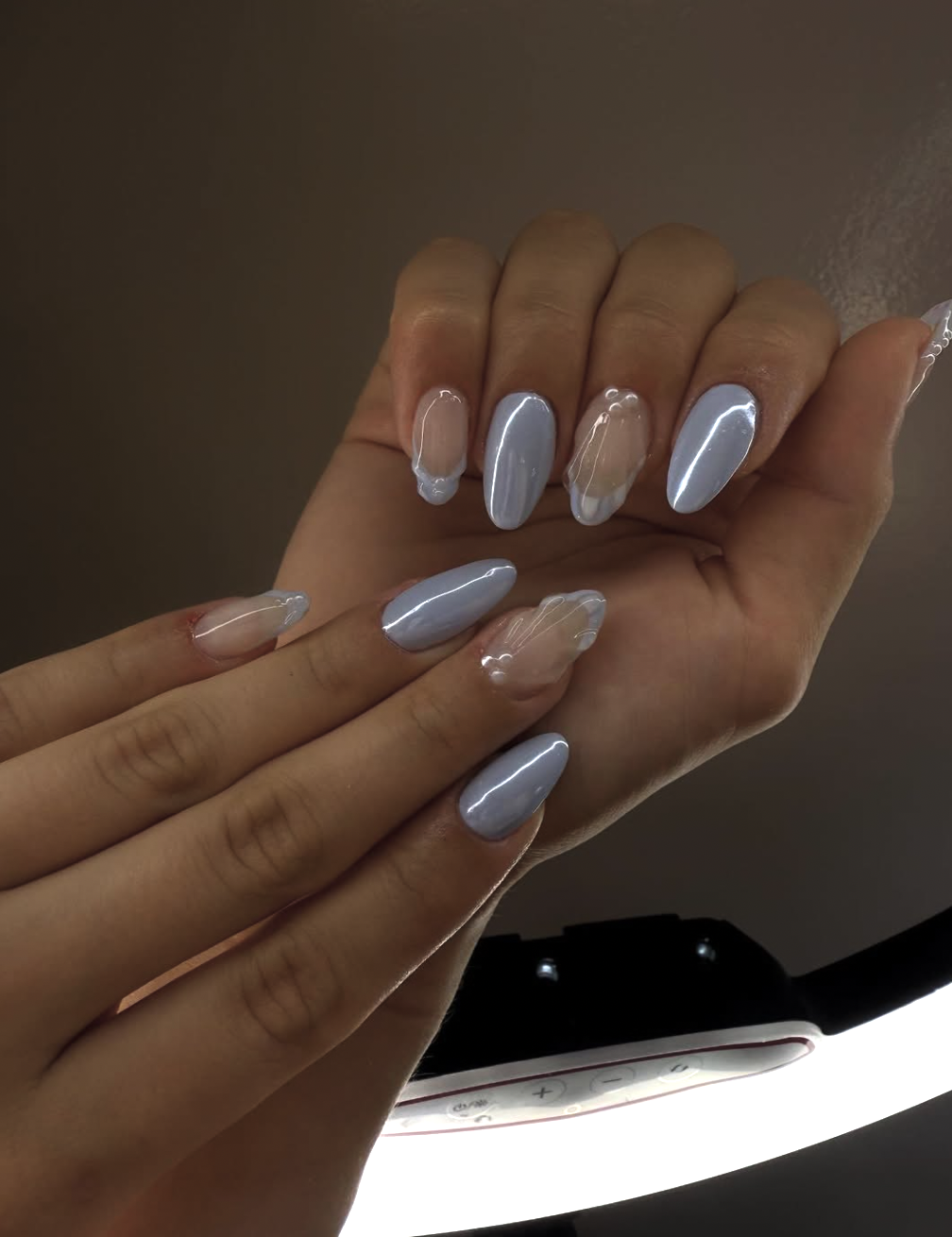 Long almond-shaped nails with a light powder blue base and a reflective, iridescent chrome finish.