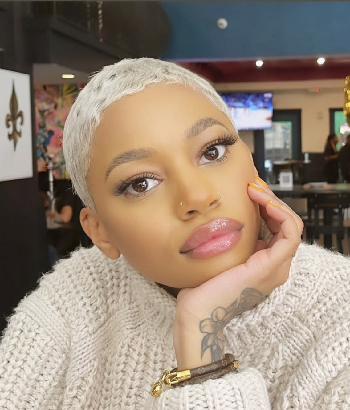 Jenn Longstreet with a platinum blonde shaved head and styled edges, wearing a white cable knit sweater and showcasing the angular bone structure of a diamond face shape.