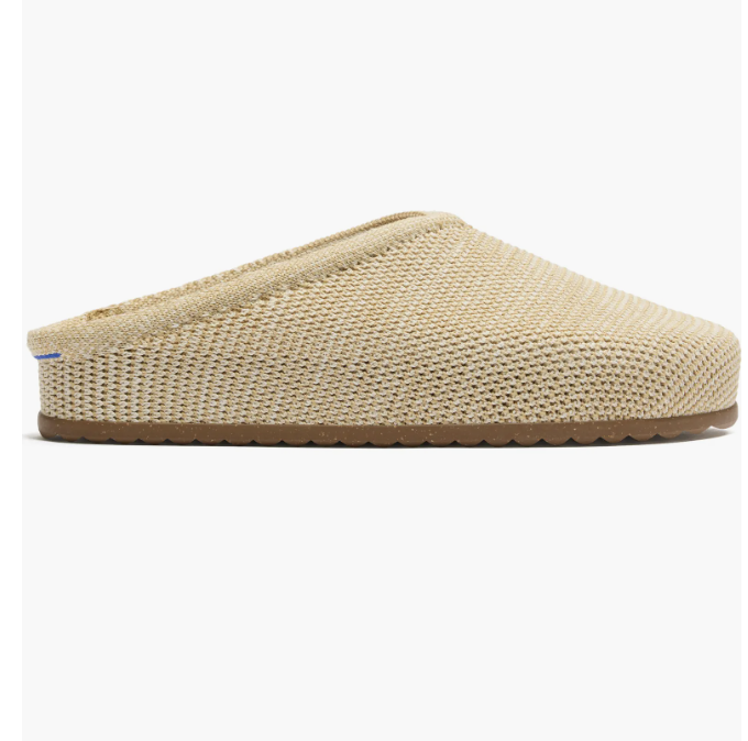 A studio product shot of a light beige, open-weave mesh slip-on clog mule with a flat, low-profile brown rubber sole.