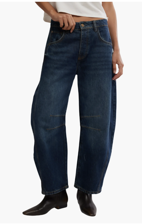 A product photo of the Free People Good Luck Mid Rise Barrel Jeans in a dark wash, styled with a white t-shirt and dark brown leather boots to showcase the curved, architectural silhouette.
