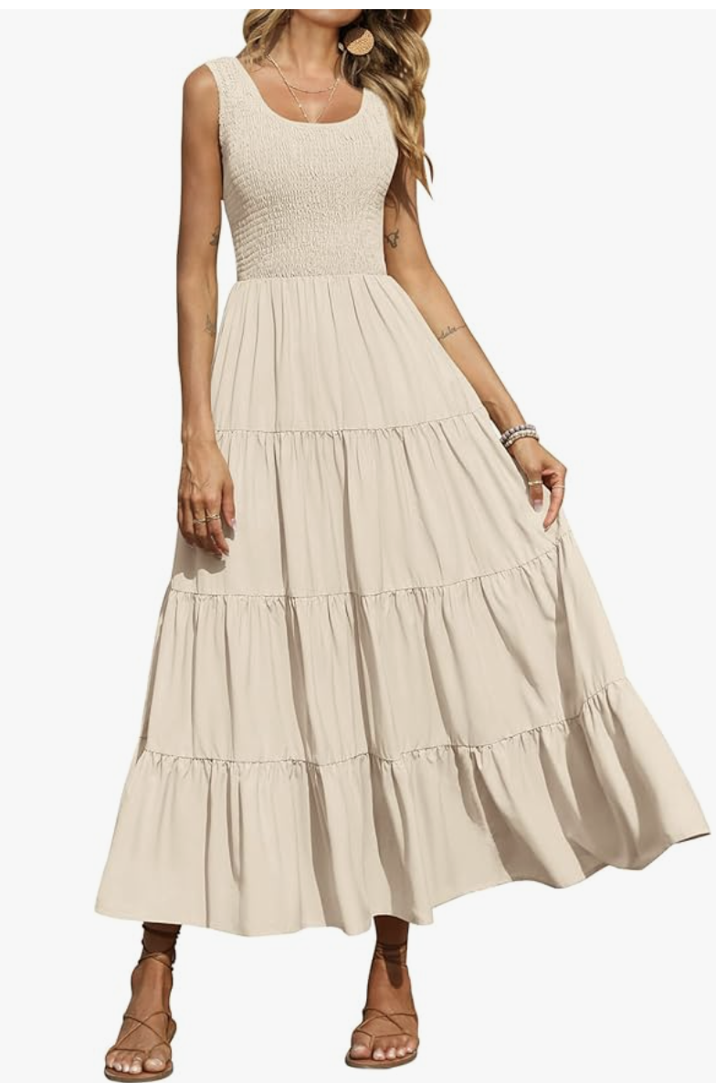A woman wearing a cream-colored sleeveless maxi dress with a smocked bodice, square neckline, and a long tiered flowy skirt.