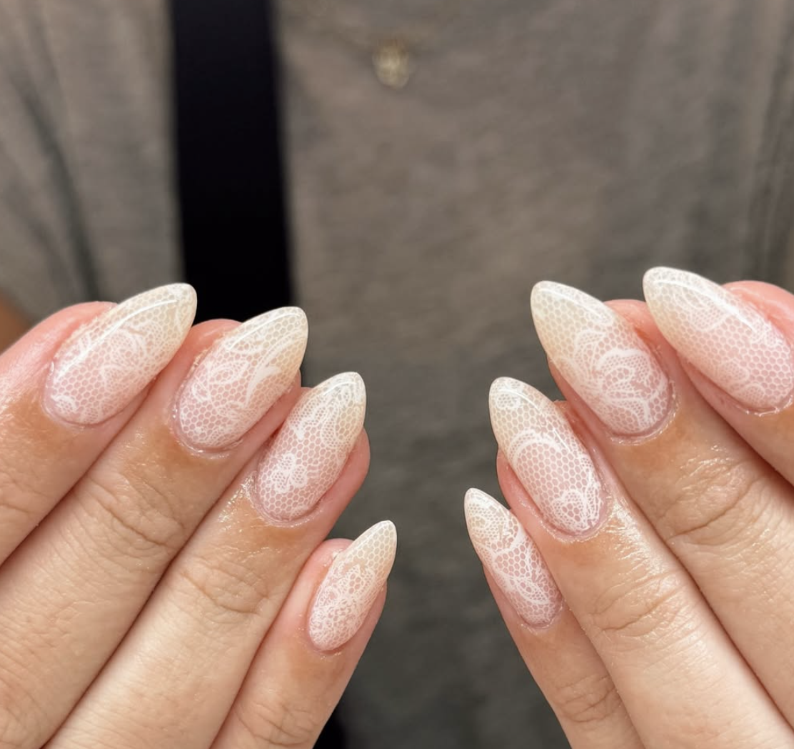 Long almond-shaped nails with full-coverage white lace patterns over a sheer nude base.