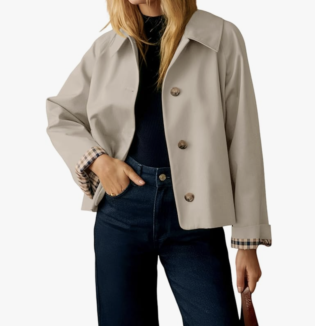 A woman wearing a khaki-colored short trench jacket with a button-down front and a classic collar, styled over a black top and dark-wash jeans for a sophisticated spring look for women in their 50s.