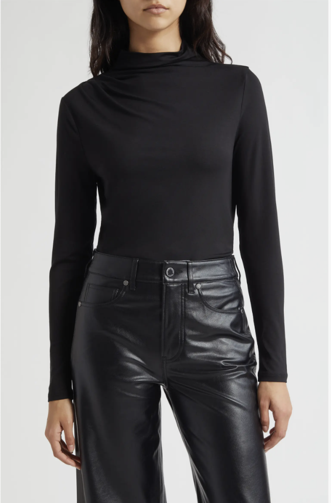 A woman wearing a sleek black mock-neck long-sleeve top styled with dark tailored leather trousers for a modern work outfit.