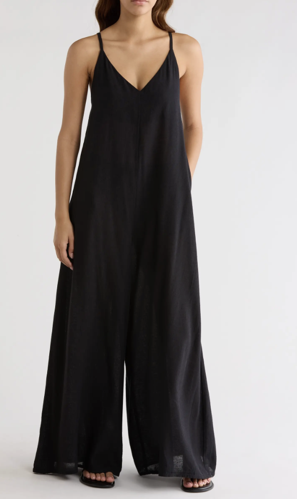 Front view of a person wearing a relaxed-fit, wide-leg black jumpsuit with thin spaghetti straps against a white background.