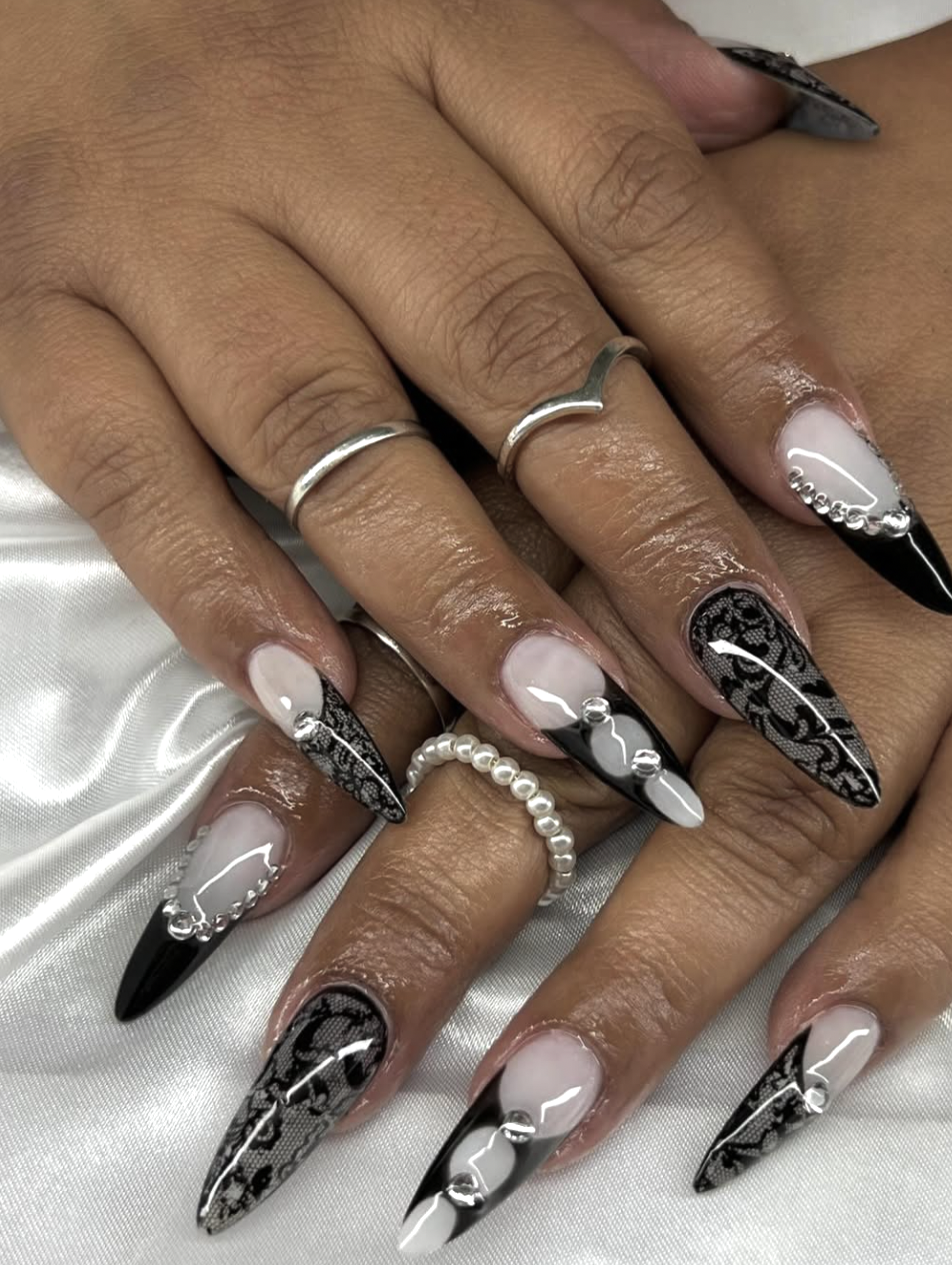 Long coffin-shaped acrylic nails with a black lace pattern over a sheer nude base.