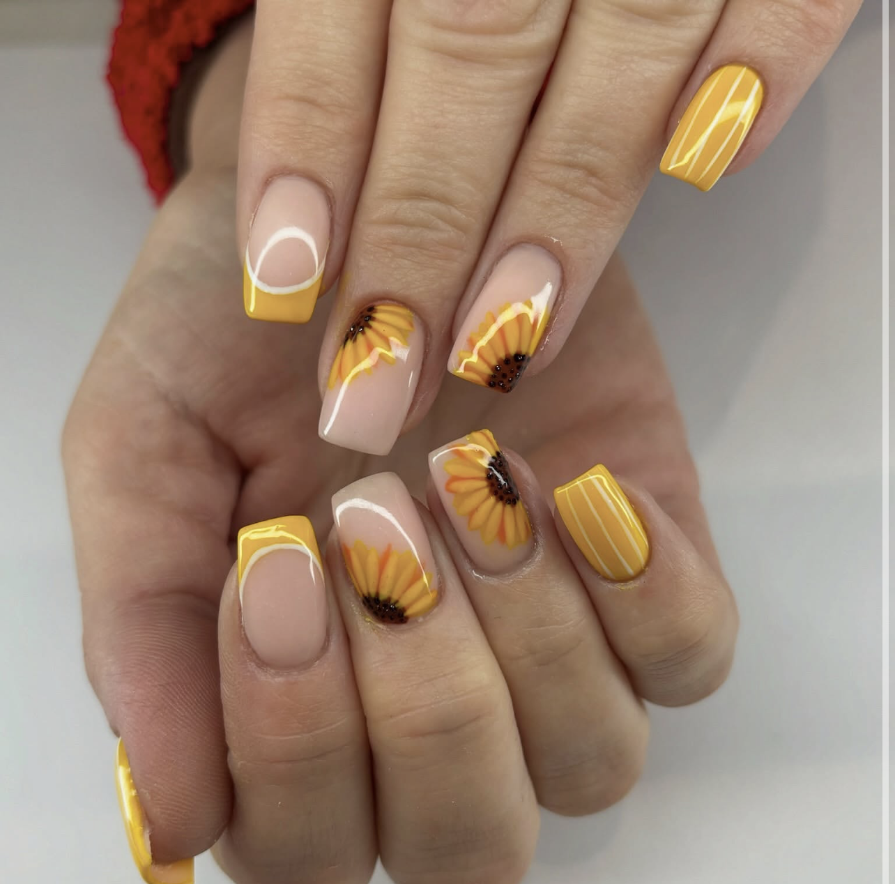 A close-up of almond-shaped nails featuring a mix of vibrant yellow polish and hand-painted sunflower designs with dark centers, representing the top summer nail trends.