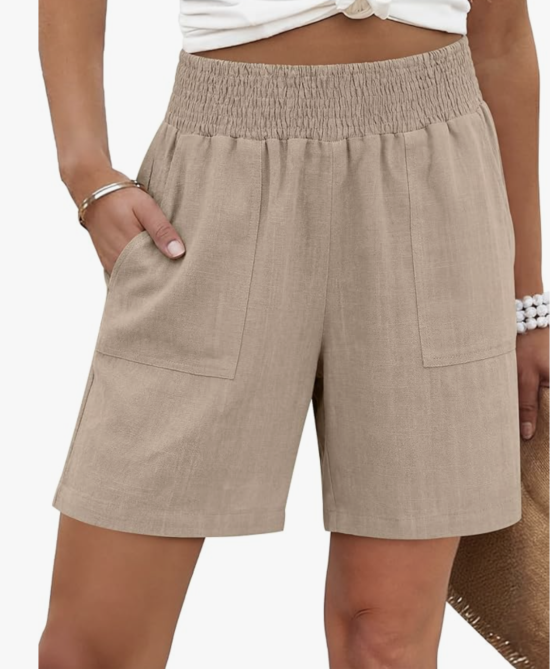 A close-up of a woman wearing tan linen-blend shorts with a smocked elastic waistband and large front patch pockets, styled for a casual summer look.