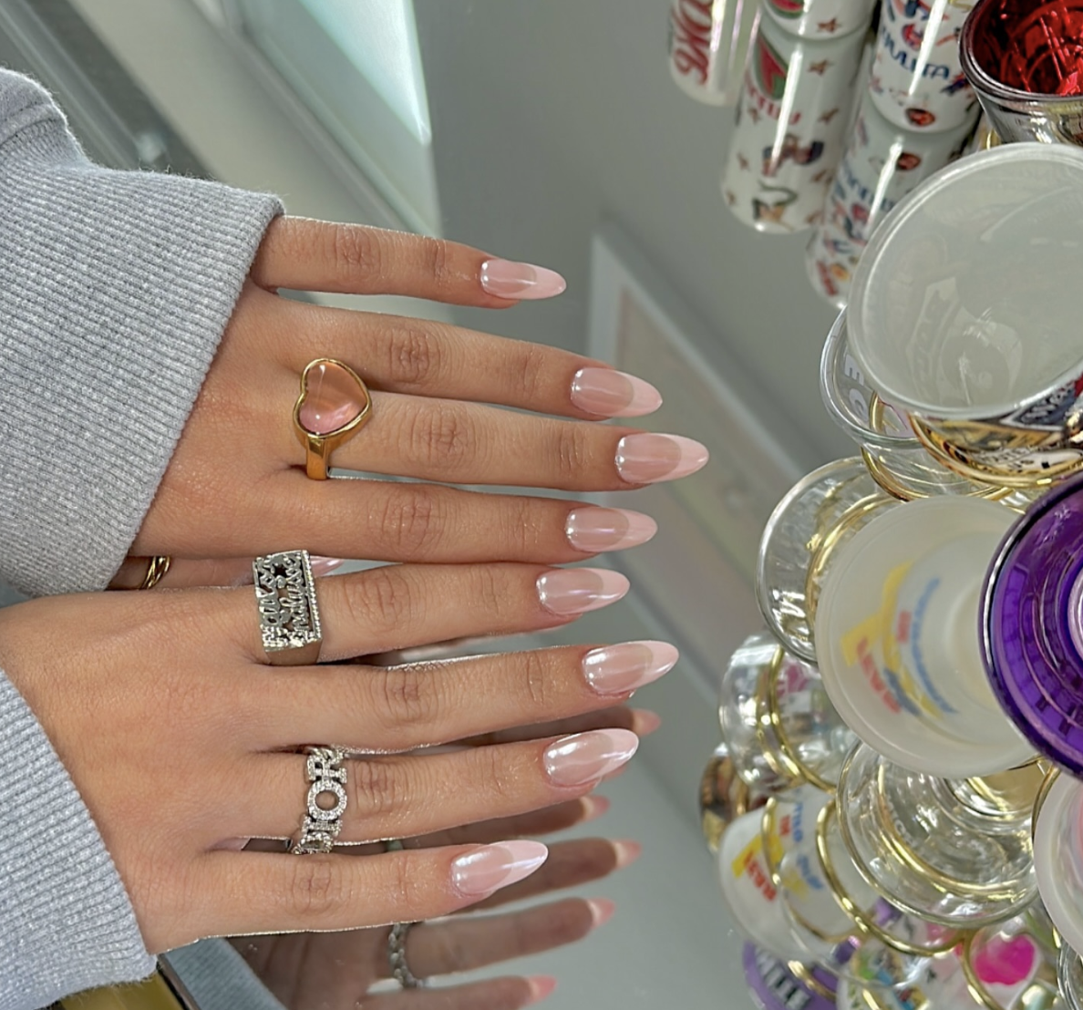 A close-up of almond-shaped nails with a sheer pink base and a soft, iridescent pearl chrome finish.