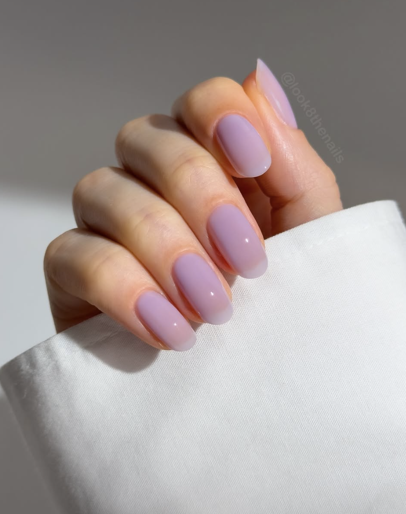 A close-up of short nails featuring a glossy, translucent lavender jelly polish manicure against a crisp white backdrop.