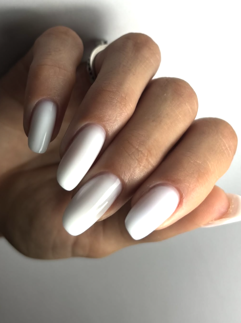 A milky white Italian manicure on short natural nails, featuring translucent polish painted with slim unpainted sidewalls to create a longer appearance.